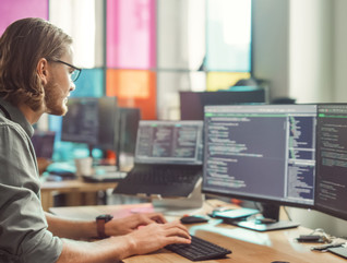 IT employee looks at code on two monitors