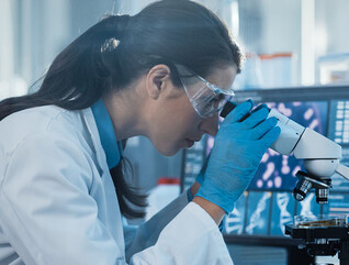 scientist looks through microscope in lab