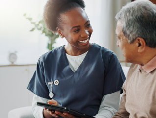 nurse and older adult talk on couch with tablet