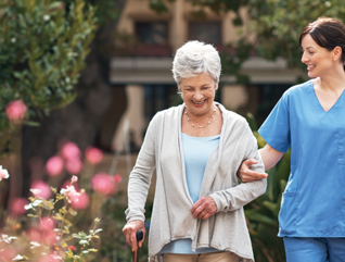 nurse walks with senior woman through a garden