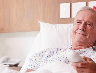 man in hospital bed uses remote to watch tv