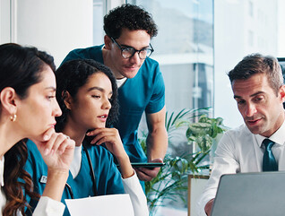 medical and IT team collaborate at table in front of laptop