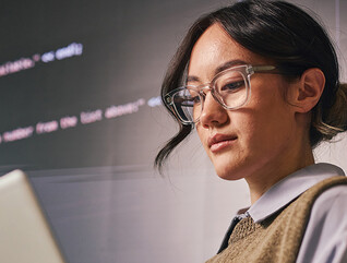 woman wearing glass holds laptop in front of wall of code