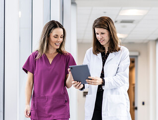 two clinicians walking down hallway looking at a tablet
