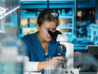 scientist looks through microscope in lab
