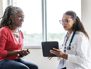 doctor talks to patient in exam room while holding a tablet
