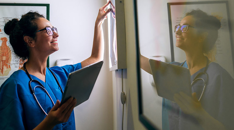 Side view of smiling middle aged nurse checking X-ray in a doctors office.
