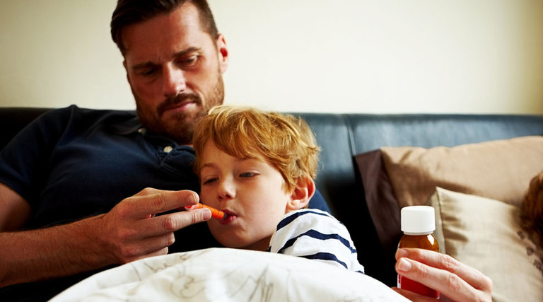Father measuring temperature of his sick son, while lying on bed