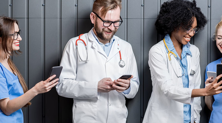 Multi ethnic group of medics standing with phones on the gray wall background