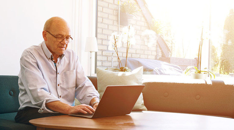 Senior man works with laptop as sun shines through windows