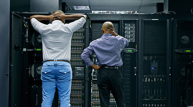 Rearview shot of two IT technicians having difficulty repairing a computer in a data center