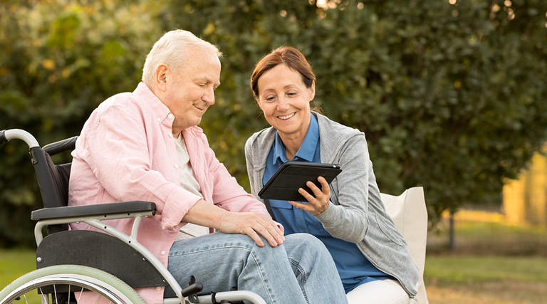 Caregiver and senior man on park bench, using digital tablet