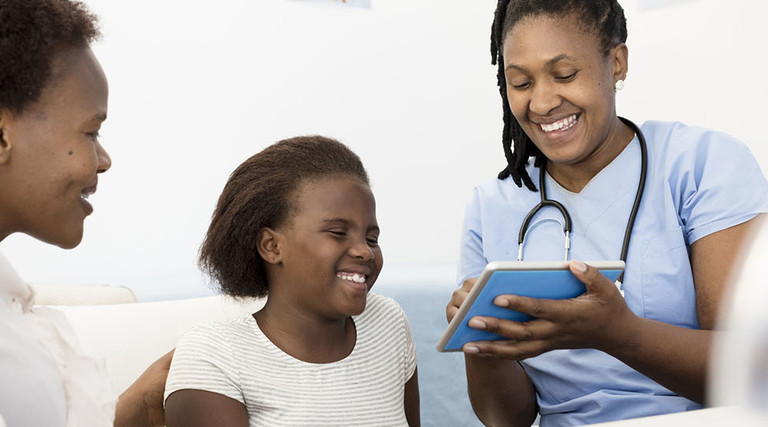 Female Doctor explaining test results on a digital tablet to a Mother & child in her consultation room at daytime.