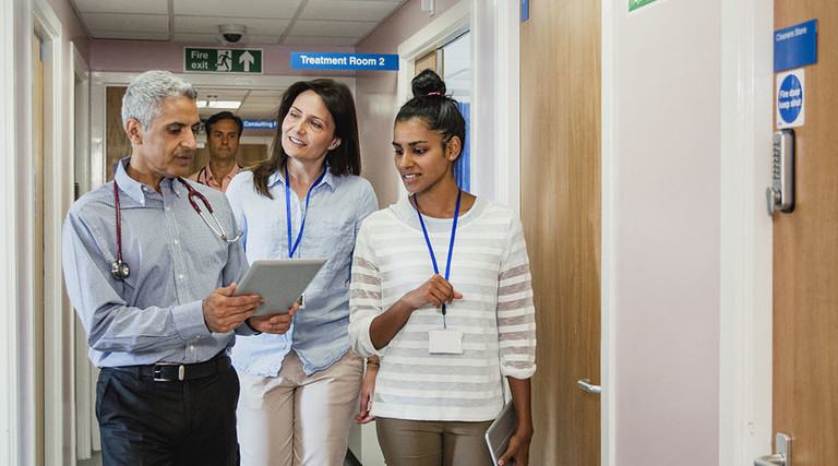 Three doctors meet in the corridor and chat along the way looking at a digital tablet