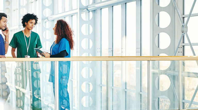 Three diverse medical professionals talking in modern hospital corridor