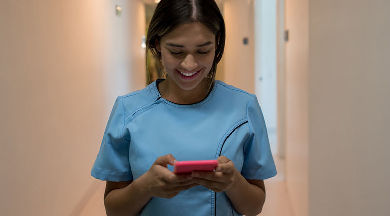 Latin american nurse walking through the hospital's corridor chatting on her smartphone smiling very happy
