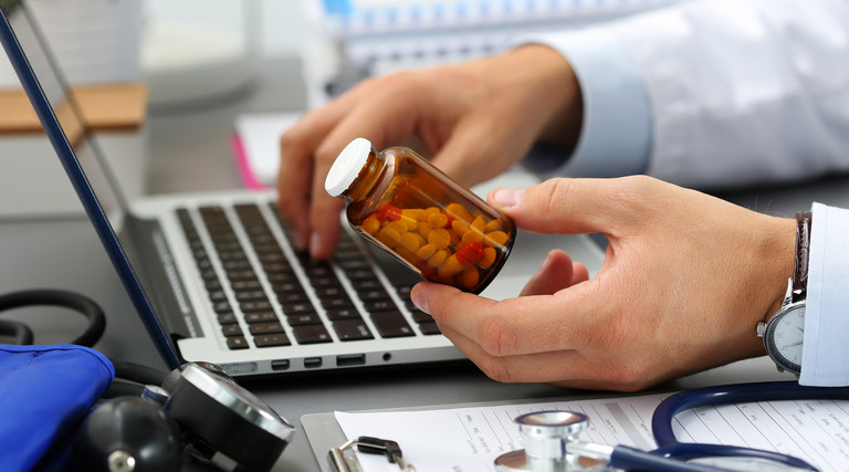 Male medicine doctor hands hold jar of pills and type something on laptop computer keyboard.