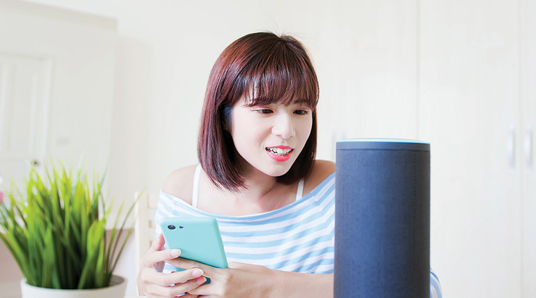 Woman with phone in hand speaking to a voice device.