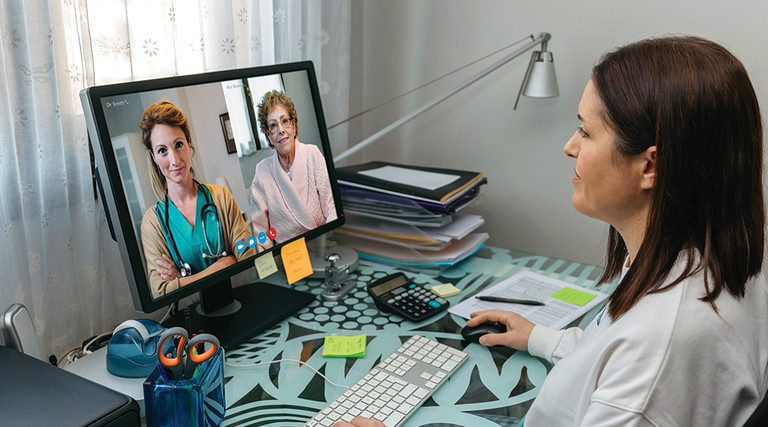 Doctor at desk speaking with patient through video conference.
