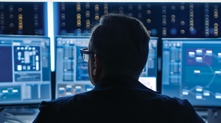 Man at desk looking at 3 computer monitors.