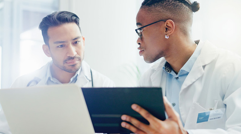 two doctors discuss treatment plans over laptop and tablet