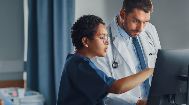 nurse and physician collaborate over desktop computer in patient room