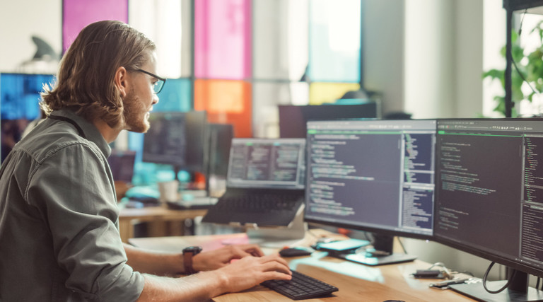 IT employee looks at code on two monitors