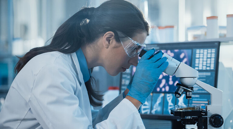scientist looks through microscope in lab