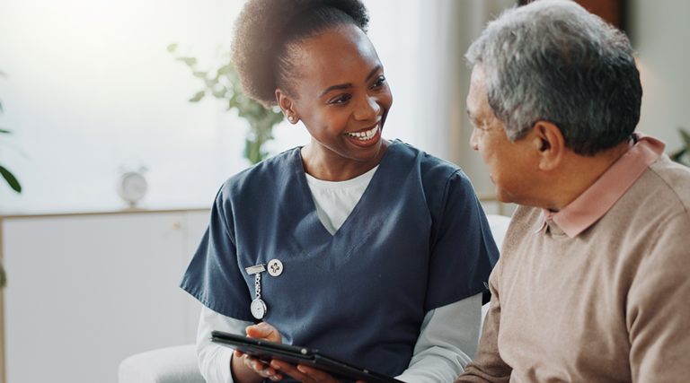 nurse and older adult talk on couch with tablet
