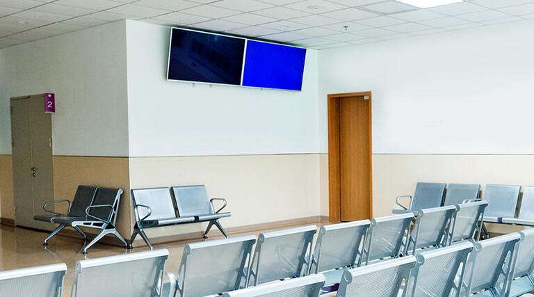 Empty seats in hospital waiting room with a television monitor.