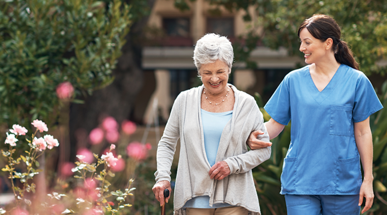 nurse walks with senior woman through a garden