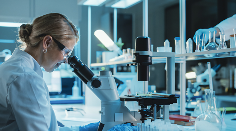 scientist looks through microscope in lab