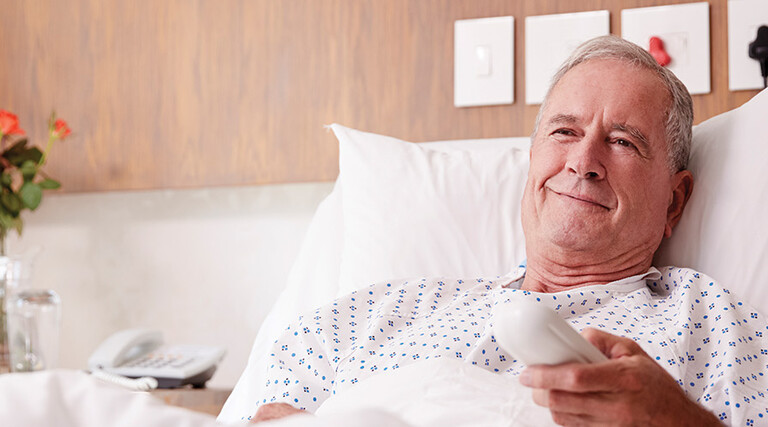 man in hospital bed uses remote to watch tv