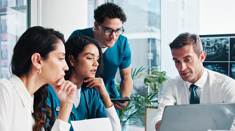 medical and IT team collaborate at table in front of laptop