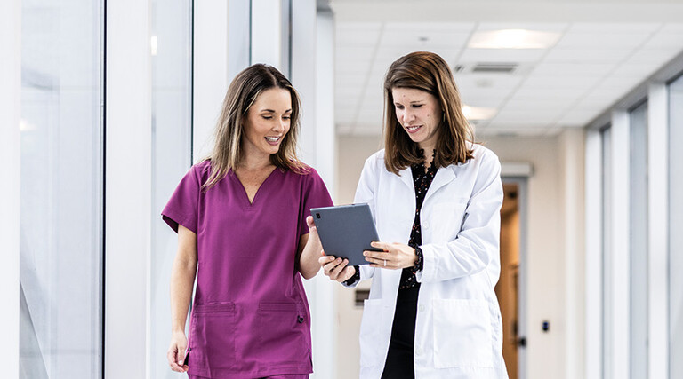 two clinicians walking down hallway looking at a tablet