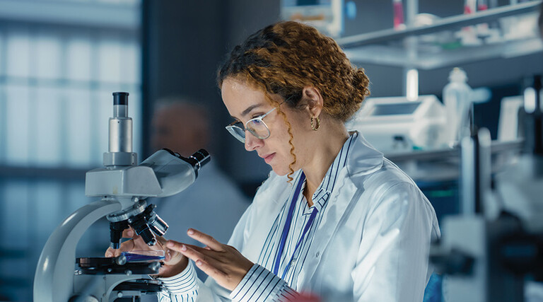 healthcare researcher looks through microscope in dark lab