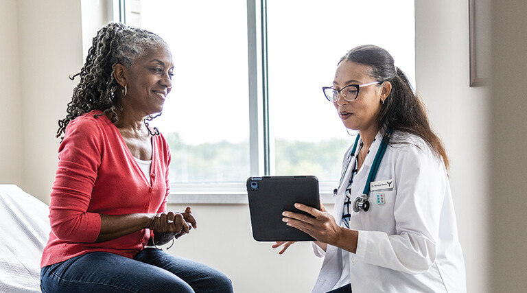 doctor talks to patient in exam room while holding a tablet