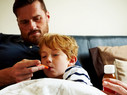 Father measuring temperature of his sick son, while lying on bed