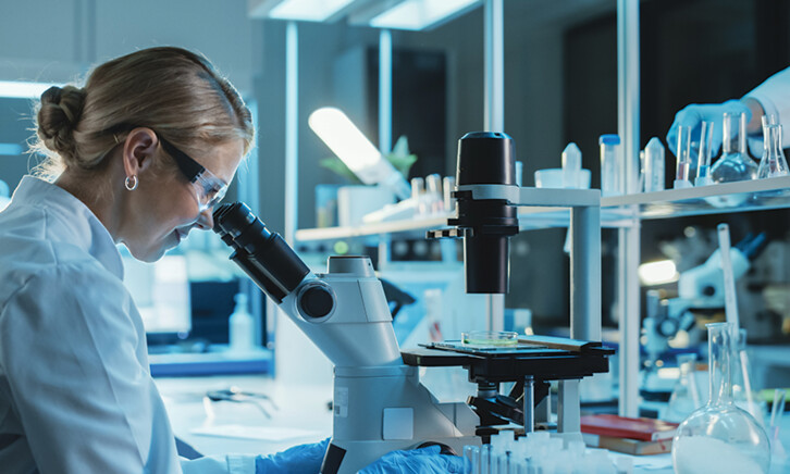 scientist looks through microscope in lab