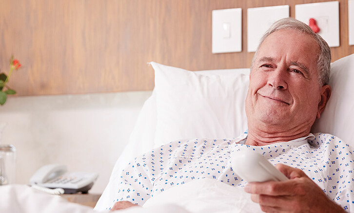 man in hospital bed uses remote to watch tv