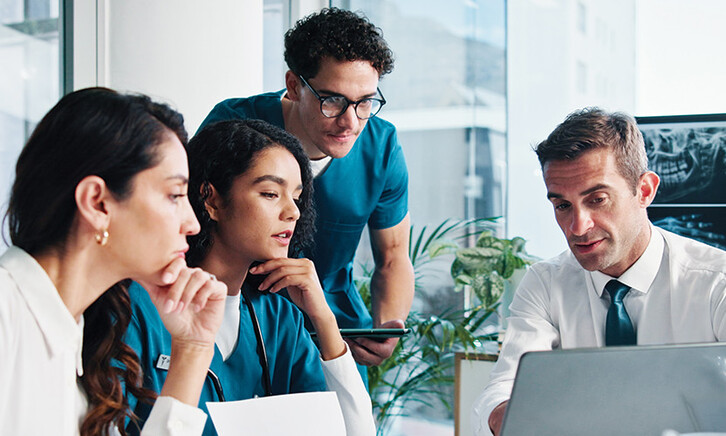 medical and IT team collaborate at table in front of laptop