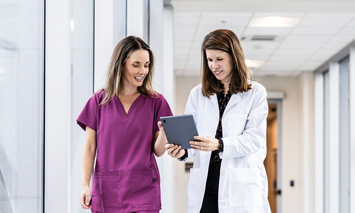 two clinicians walking down hallway looking at a tablet