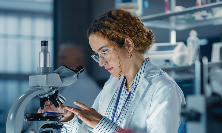 healthcare researcher looks through microscope in dark lab