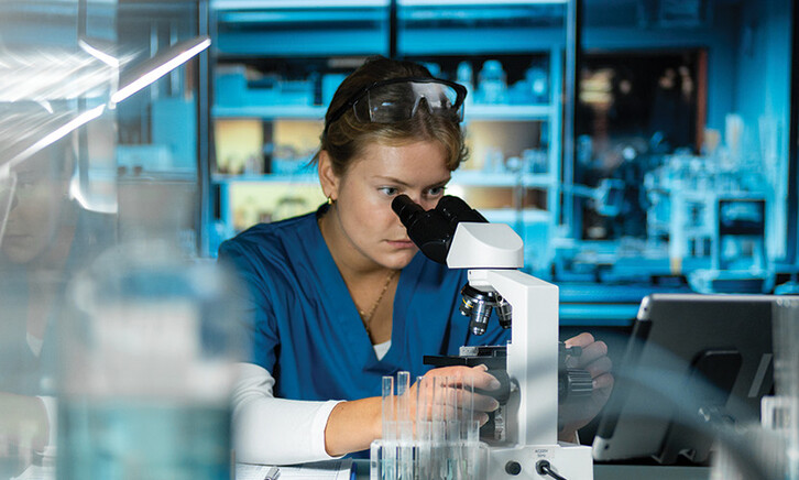 scientist looks through microscope in lab