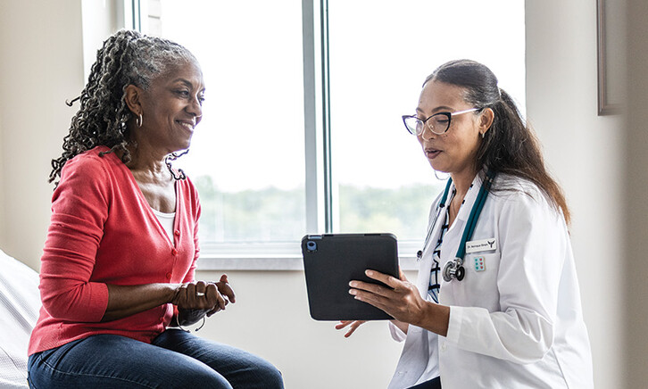 doctor talks to patient in exam room while holding a tablet