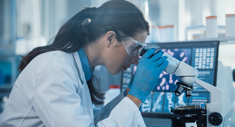 scientist looks through microscope in lab