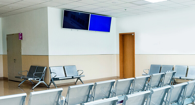 Empty seats in hospital waiting room with a television monitor.