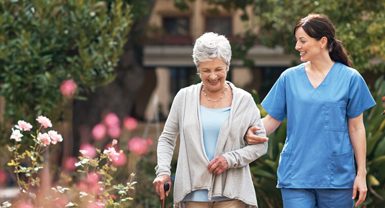 nurse walks with senior woman through a garden