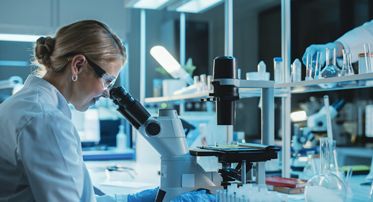 scientist looks through microscope in lab