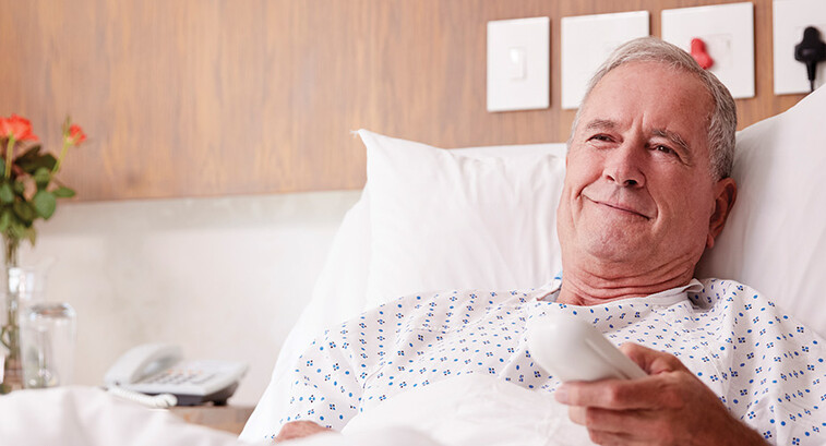 man in hospital bed uses remote to watch tv